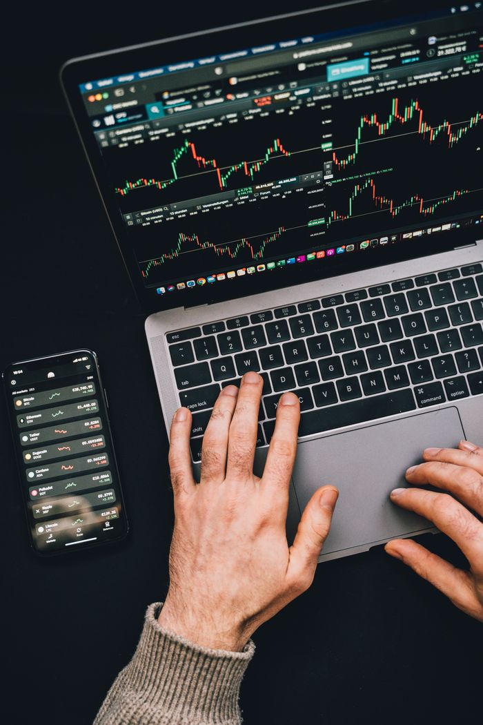 Hands at work on a laptop, with cryptocurrency charts and a smartphone screen visible, centered on digital finance.