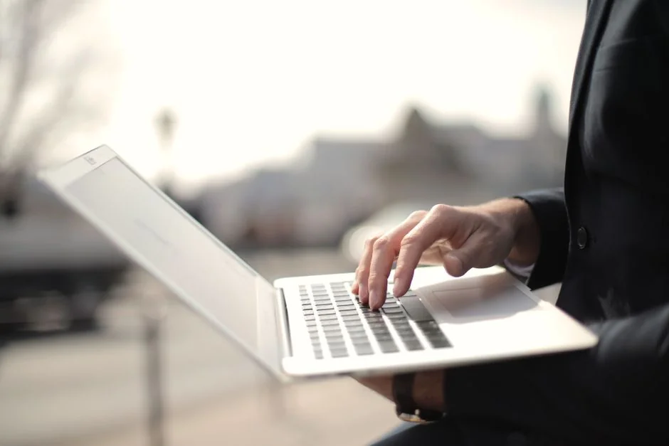 Hands using smartphone beside laptop with stock charts, showcasing digital trading.